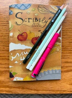 Bonnie's copy of Scribbly volume 4 on a table with pens and pencils.
